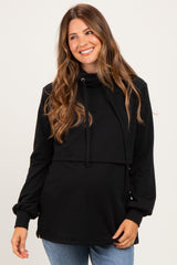 woman wearing a black maternity pullover sweatshirt with a cowl neck and drawstring detail, showing her baby bump