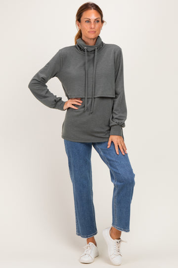 woman wearing a dark gray long sleeve cowl neck sweatshirt paired with light blue straight leg jeans and white sneakers
