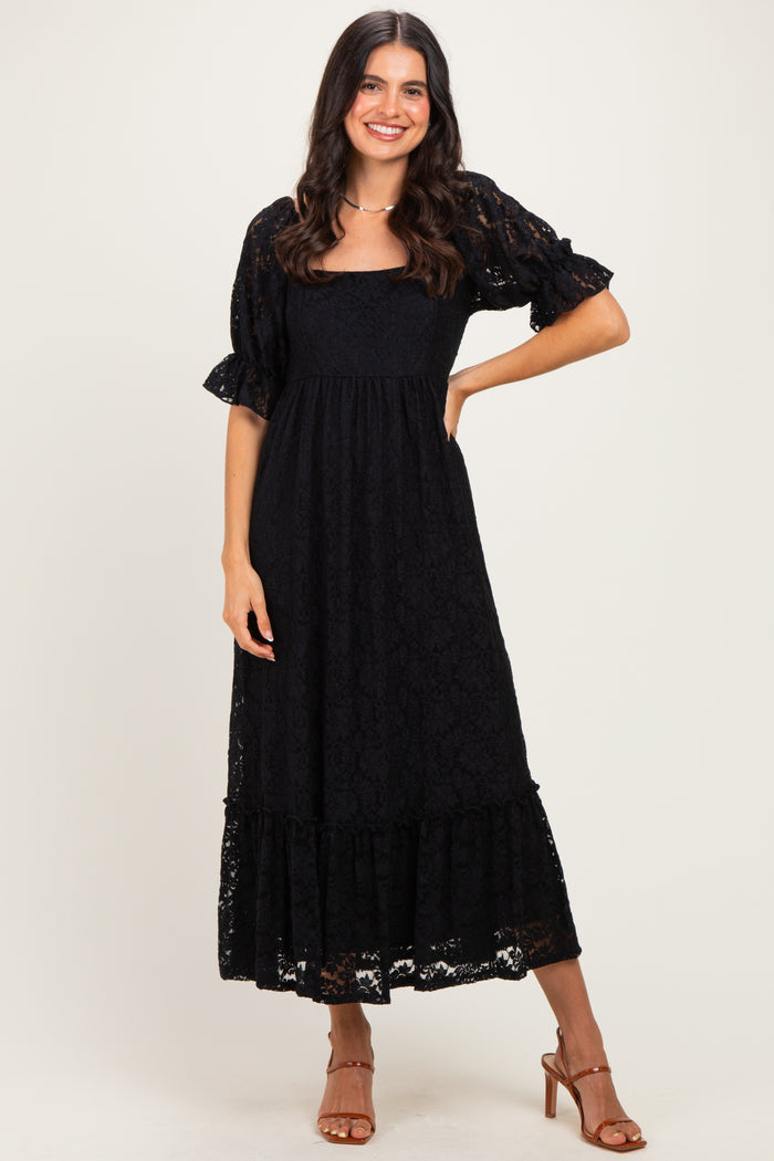 woman wearing a black lace maxi dress with flutter sleeves and a tiered hem, standing confidently and smiling