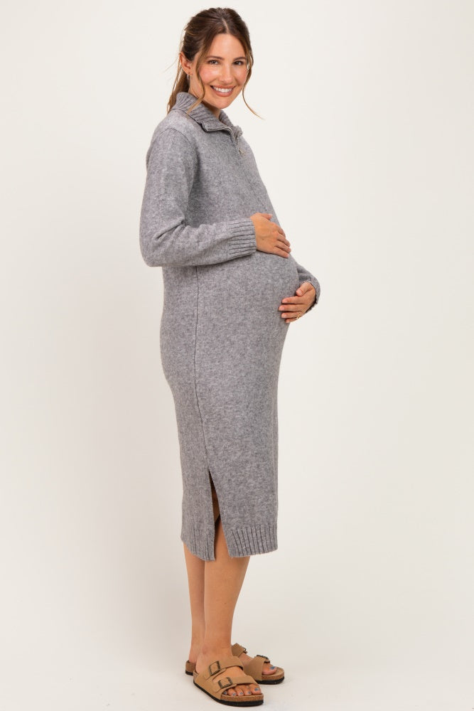 woman wearing a gray knitted maternity sweater dress with side slits and holding her baby bump