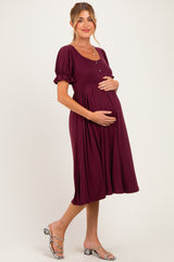 woman wearing a burgundy maternity dress with puff sleeves and buttons, holding her baby bump