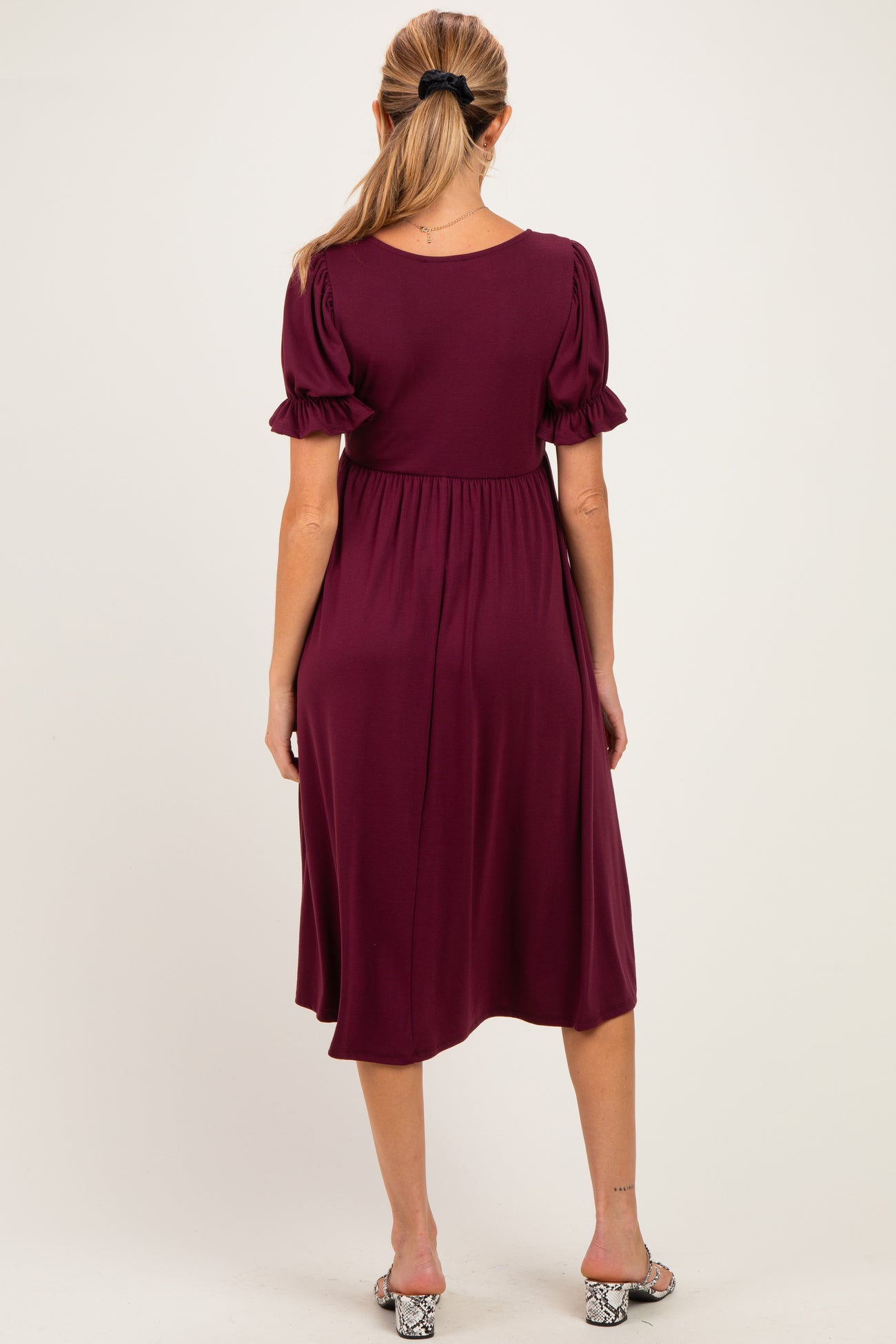 woman wearing a burgundy maternity dress with puff sleeves, showing a flowing silhouette from the back