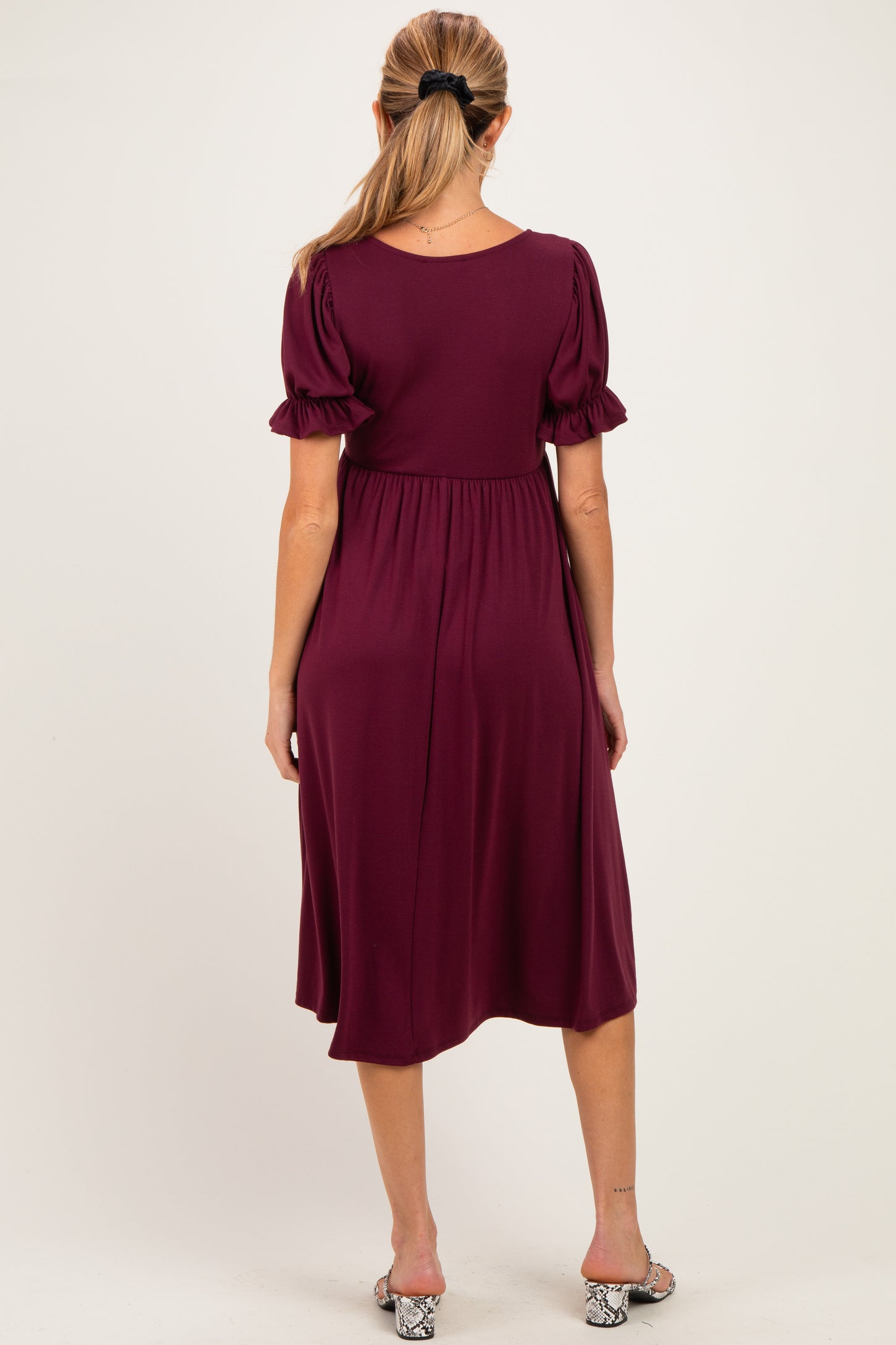 woman wearing a burgundy maternity dress with puff sleeves, showing a flowing silhouette from the back