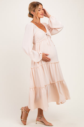 woman wearing a light pink maternity dress with long sleeves and a tiered skirt, cradling her baby bump