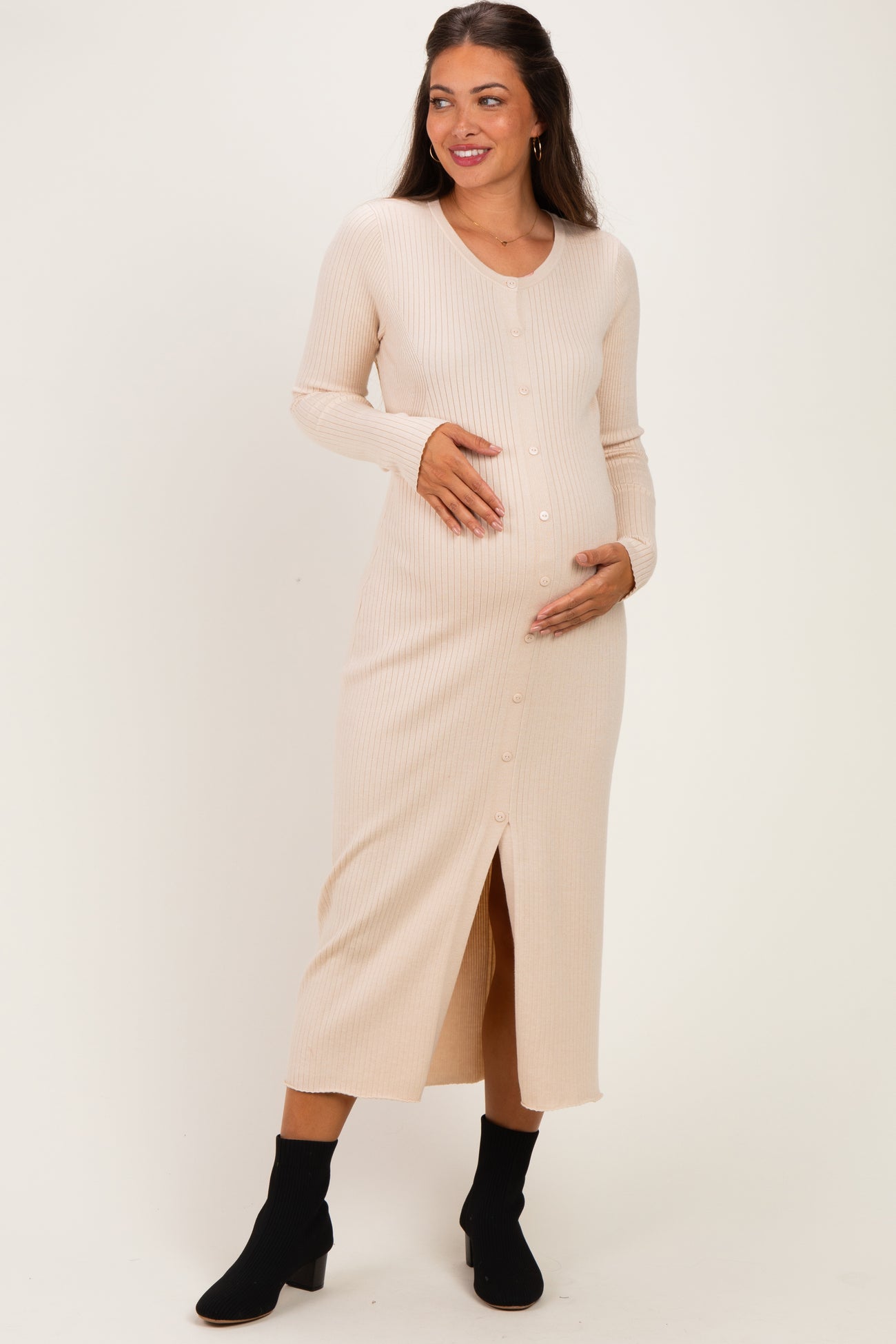 woman wearing a light beige ribbed maternity dress with a button front and slit, holding her baby bump