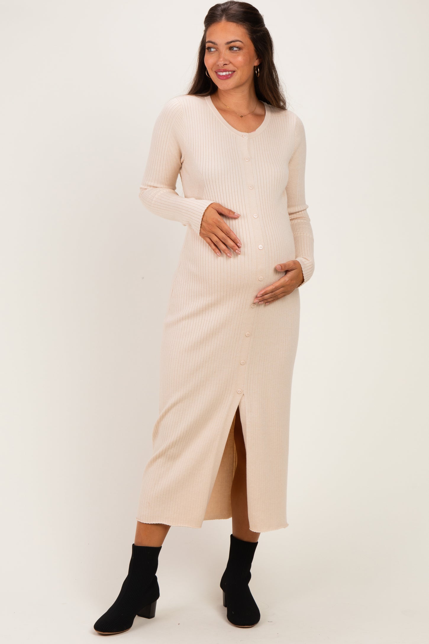 woman wearing a light beige ribbed maternity dress with a button front and slit, holding her baby bump