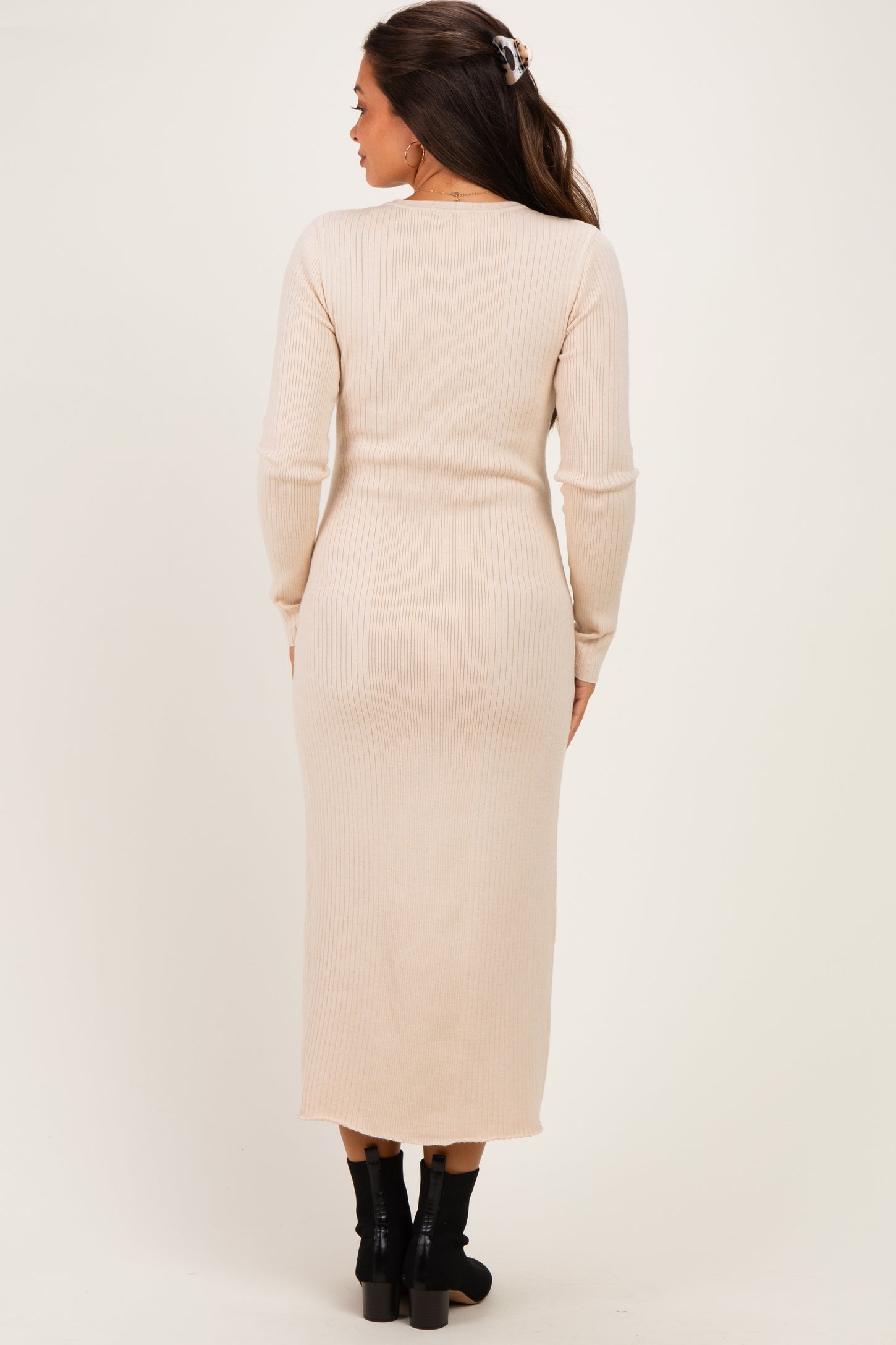 woman wearing a beige ribbed maternity dress with long sleeves, showing a fitted silhouette and midi length