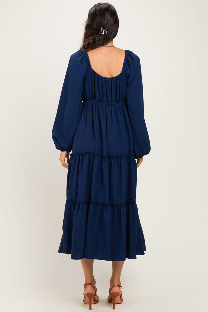 woman wearing a navy blue tiered maxi dress with long puff sleeves and a scoop back