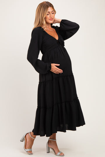 woman wearing a black tiered maternity dress with long sleeves and a baby bump visible, posing gracefully