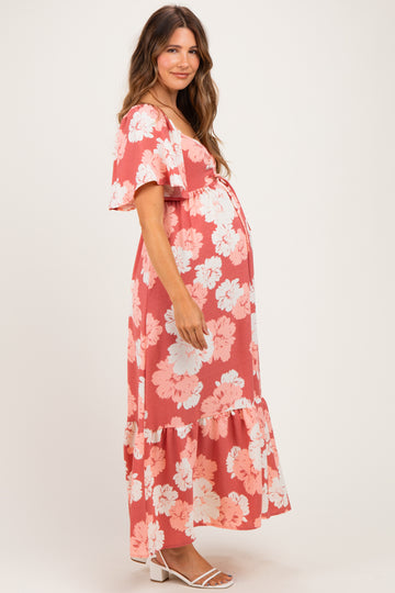 woman wearing a coral floral maternity maxi dress with short sleeves and a ruffled hem, showcasing a baby bump
