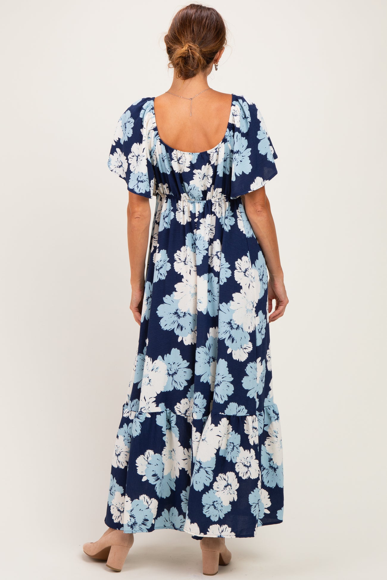 woman wearing a navy blue floral maxi dress with short sleeves and a tiered skirt, viewed from the back
