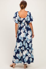 woman wearing a navy blue floral maxi dress with short sleeves and a tiered skirt, viewed from the back