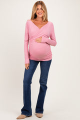 woman wearing a light pink long sleeve maternity top and blue flared jeans, holding her baby bump