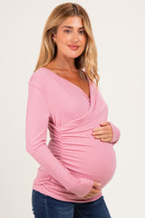 woman wearing a pink long sleeve maternity top with a wrap design and holding her baby bump