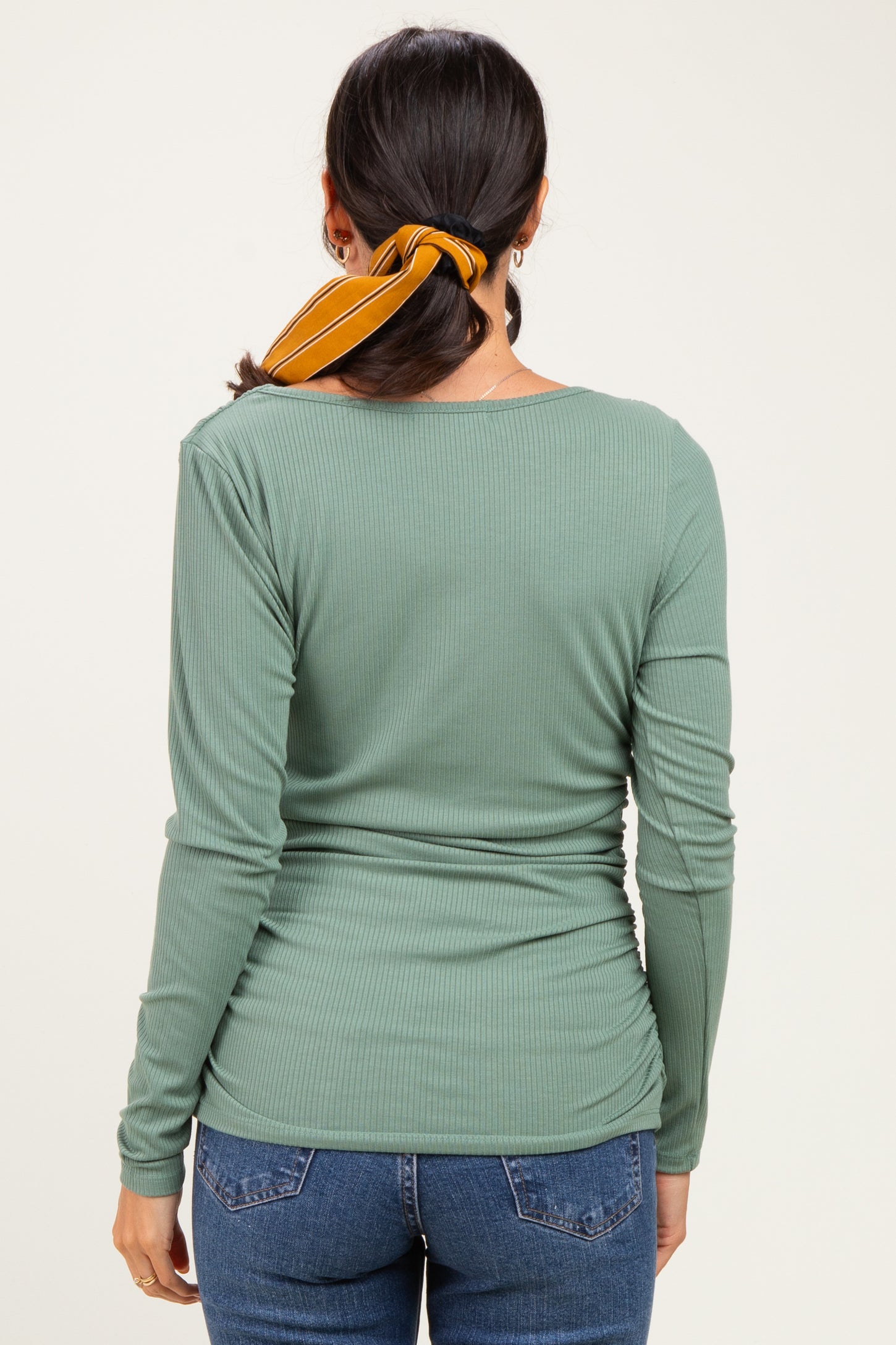 woman wearing a green ribbed long sleeve top with a scoop back and styled hair with a yellow scarf