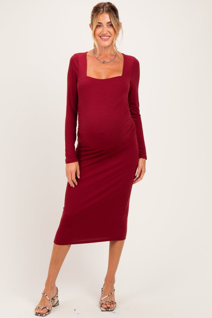 woman wearing a burgundy long sleeve maternity dress with a square neckline and fitted silhouette, showing her baby bump
