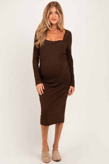 woman wearing a brown long sleeve maternity dress with a scoop neckline and fitted silhouette, highlighting her baby bump