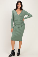 woman wearing a green long sleeve wrap dress with ruching and a v-neck, standing with one hand on her hip
