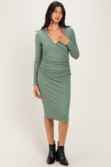 woman wearing a sage green long sleeve wrap dress with ruching detail and a fitted silhouette