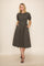 woman wearing a dark gray midi dress with puff sleeves and pockets, standing against a neutral background