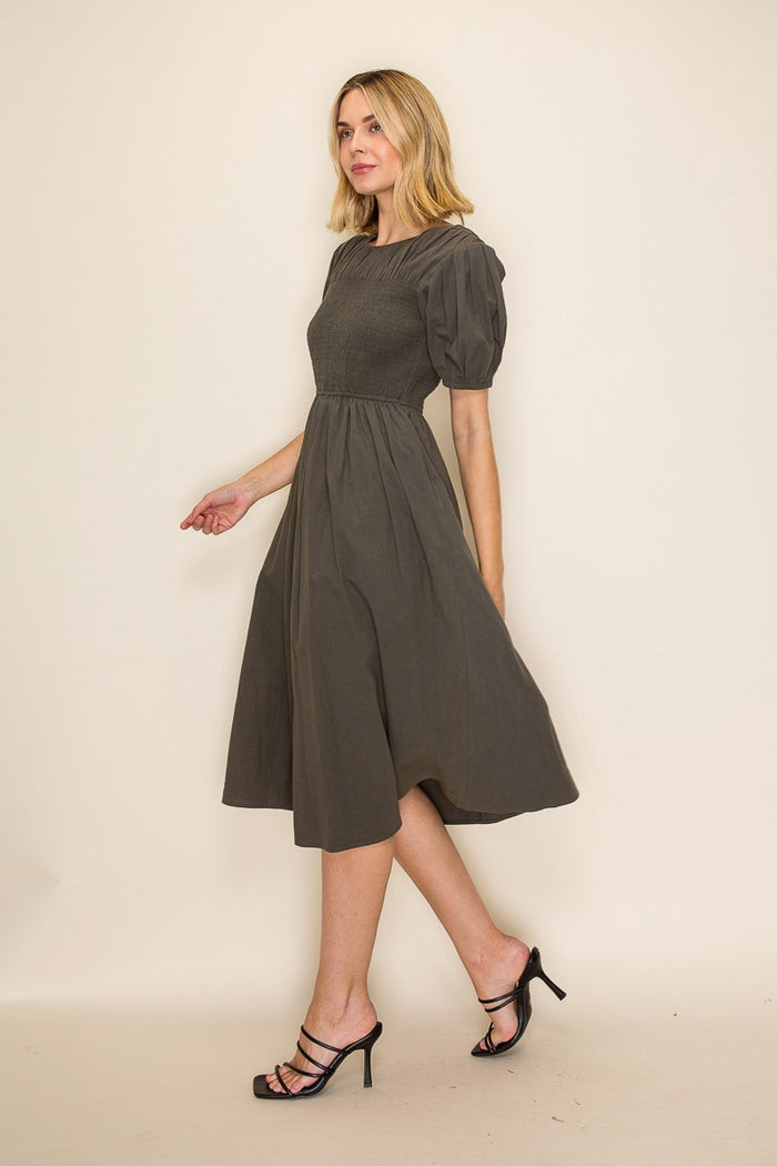 woman wearing an olive green puff sleeve midi dress with a fitted bodice and flared skirt, walking confidently