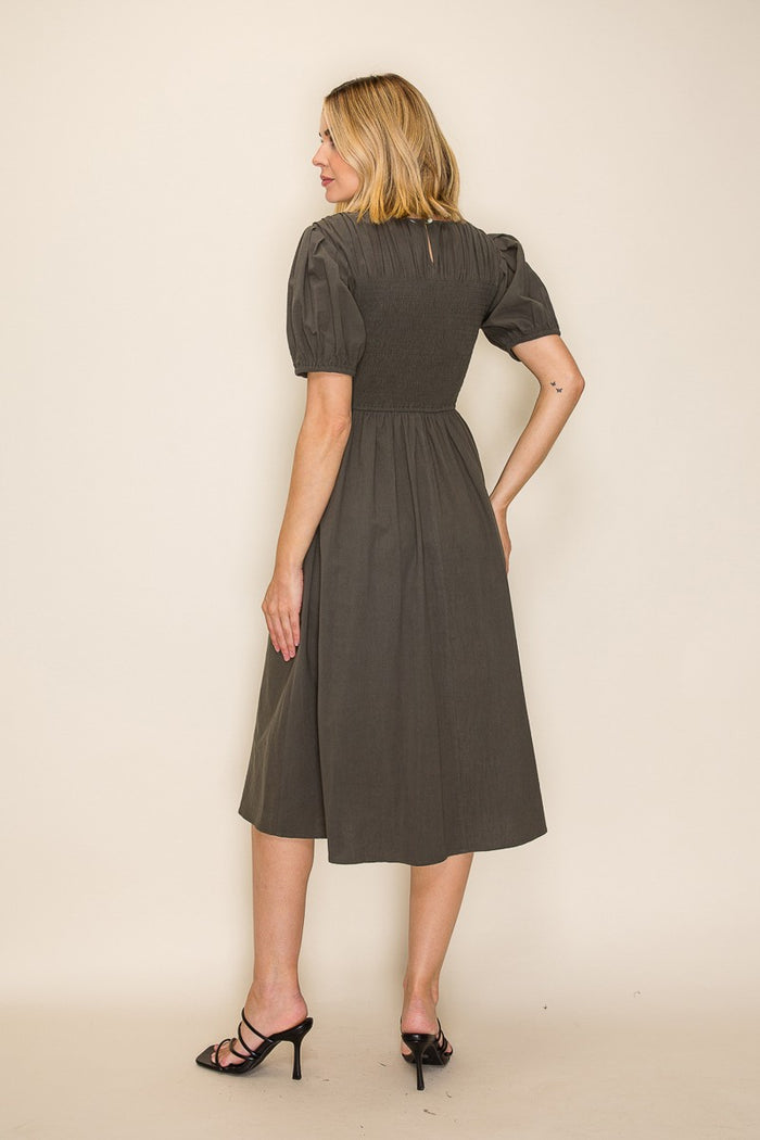 woman wearing a dark green midi dress with puff sleeves and a smocked back, standing with her back to the camera