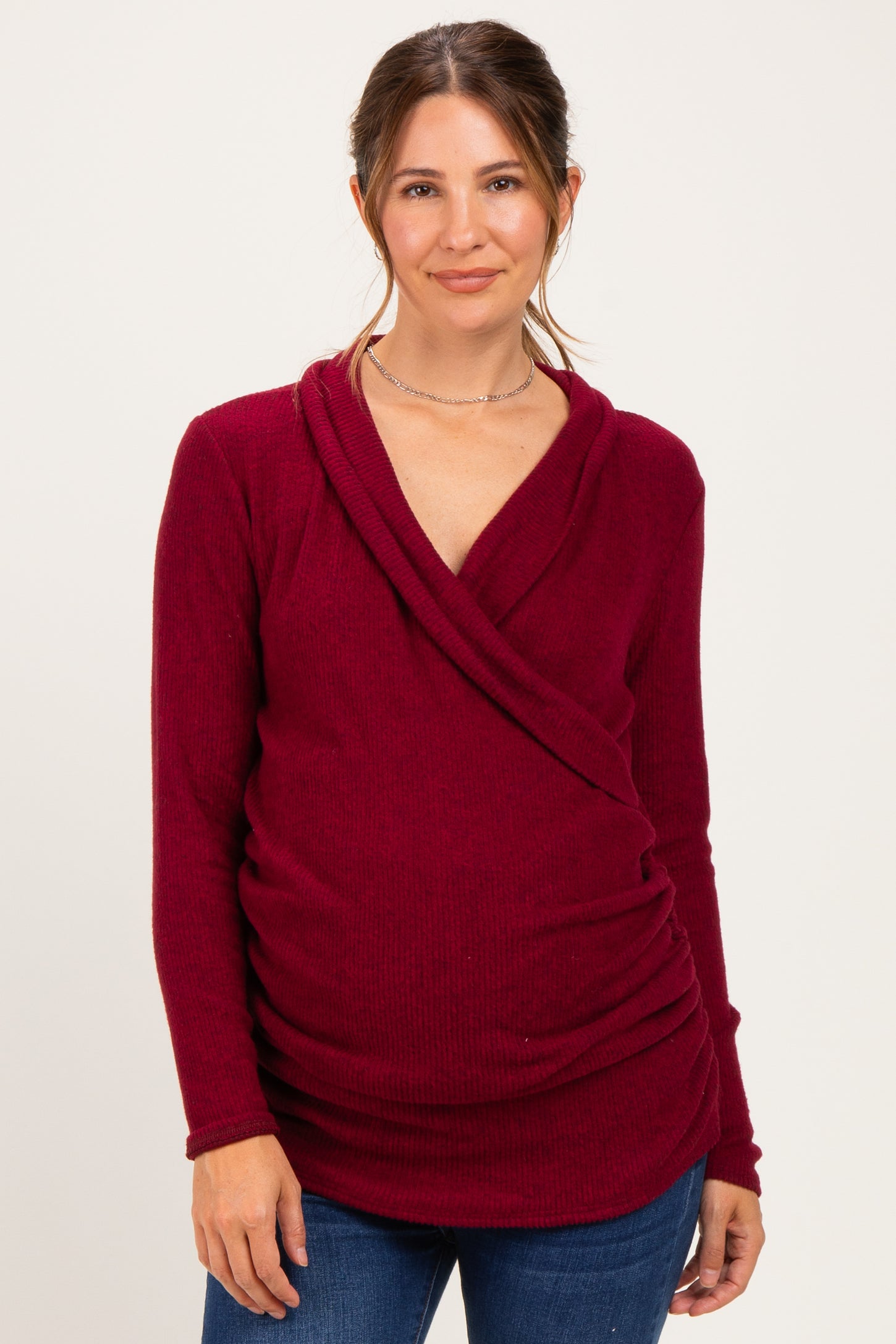 woman wearing a burgundy long sleeve maternity top with a crossover design and ruched sides, showing a baby bump