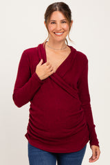 woman wearing a burgundy maternity wrap top with gathered detailing, smiling and holding her baby bump