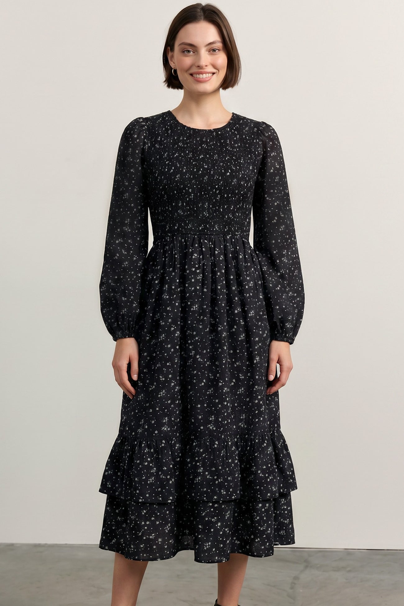 woman wearing a black floral long sleeve dress with a smocked bodice and tiered ruffle hem