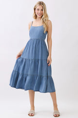 woman wearing a blue tiered denim midi dress with spaghetti straps and a flowy hemline