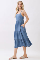 woman wearing a light blue chambray tiered midi dress with spaghetti straps and pockets