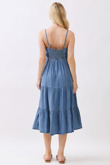 woman wearing a back view of a blue denim maxi dress with adjustable straps and smocked bodice