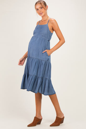 woman wearing a denim blue maternity dress with tiered ruffles and pockets, showcasing her baby bump