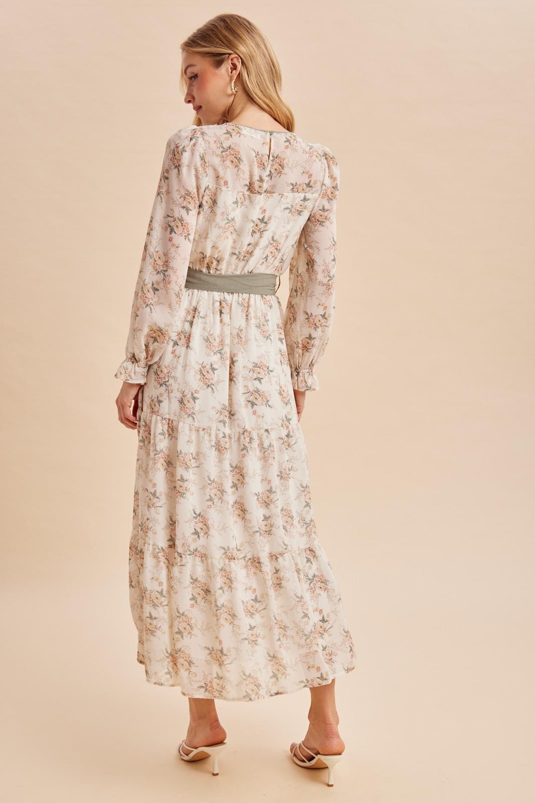 woman wearing a floral long sleeve maxi dress with a cinched waist, standing against a neutral background