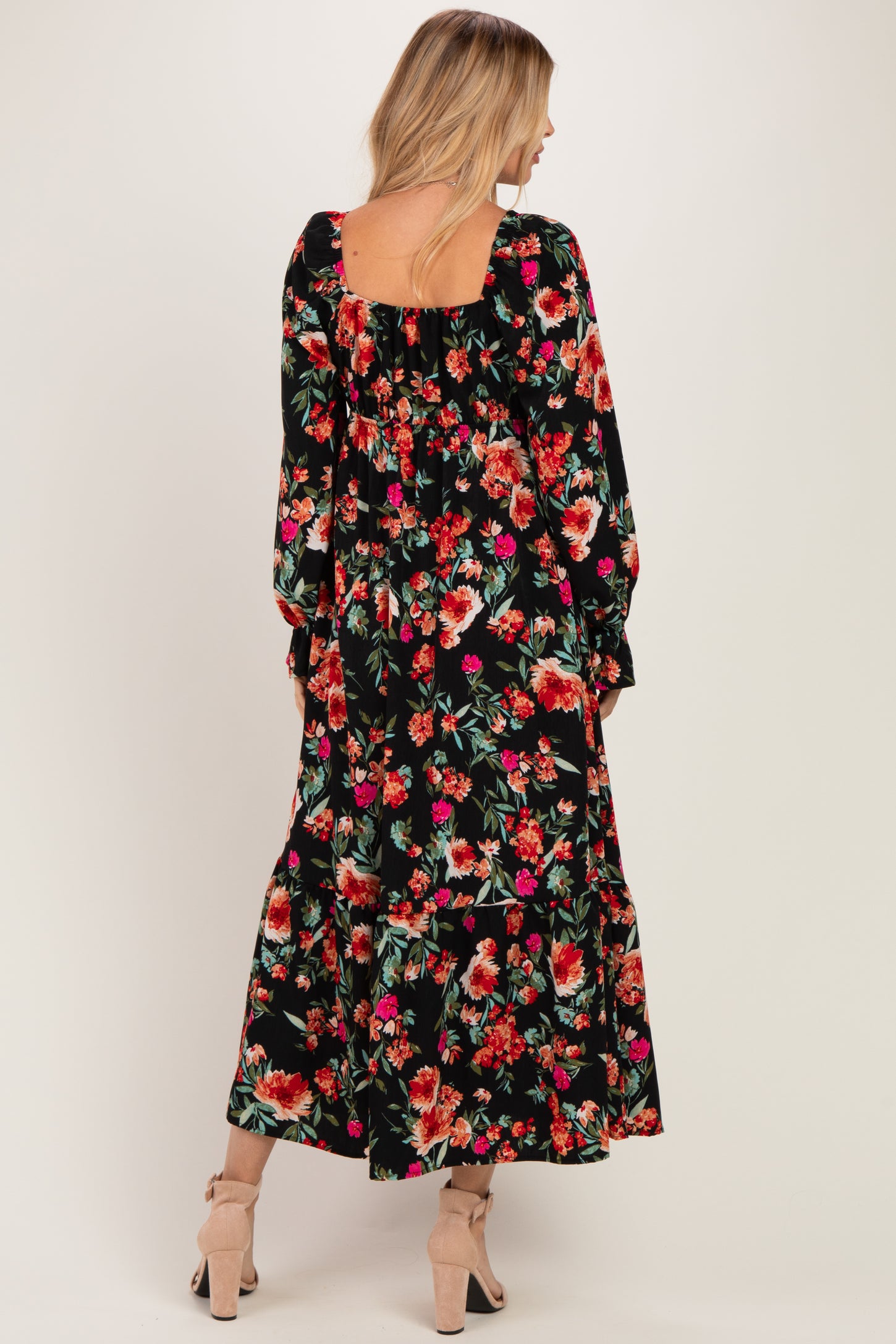 woman wearing a black floral maxi dress with long sleeves and a square back, standing and facing away from the camera