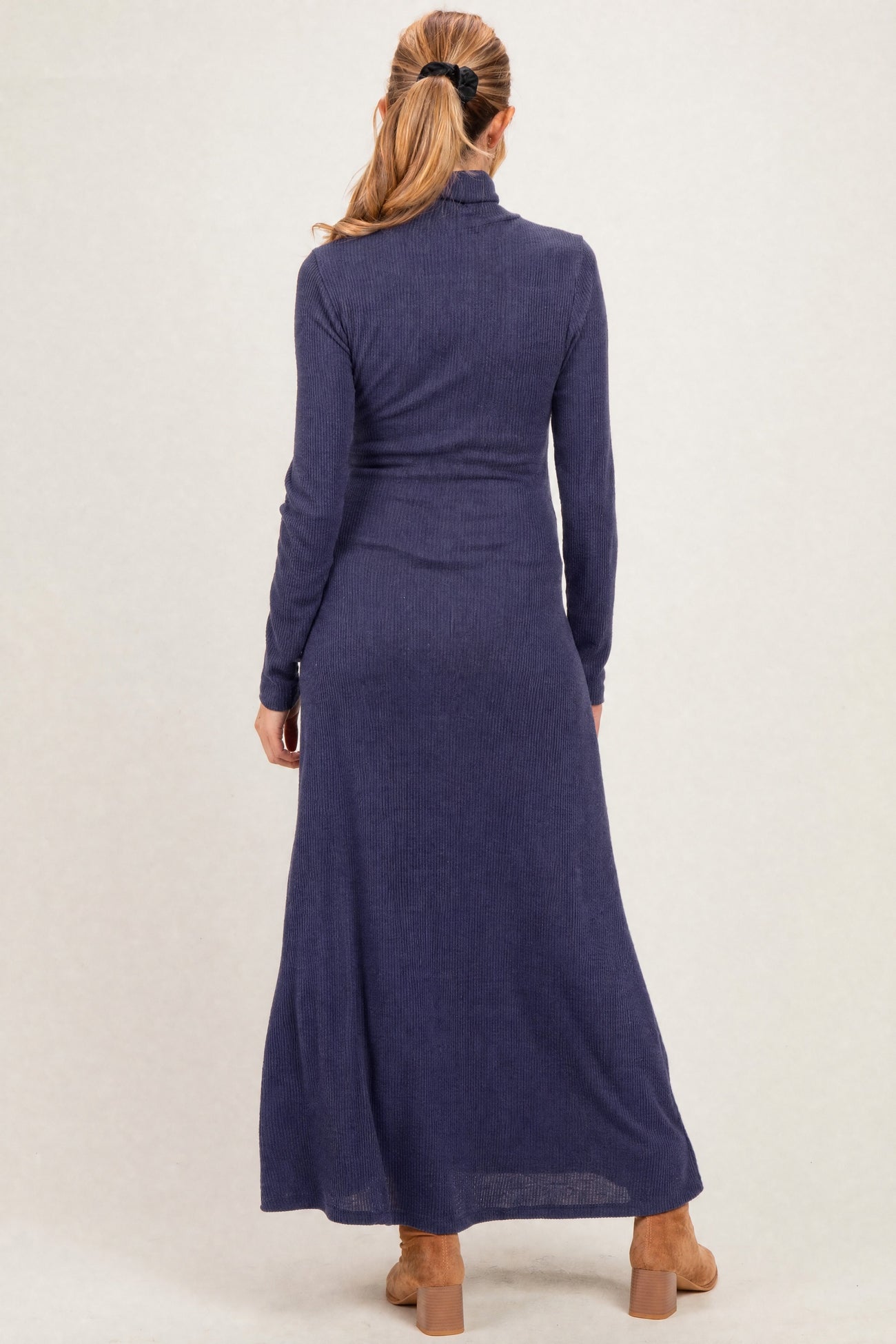 woman wearing a navy blue maternity maxi dress with long sleeves and a turtleneck, featuring a fitted waist and flowing skirt