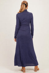 woman wearing a navy blue maternity maxi dress with long sleeves and a turtleneck, featuring a fitted waist and flowing skirt