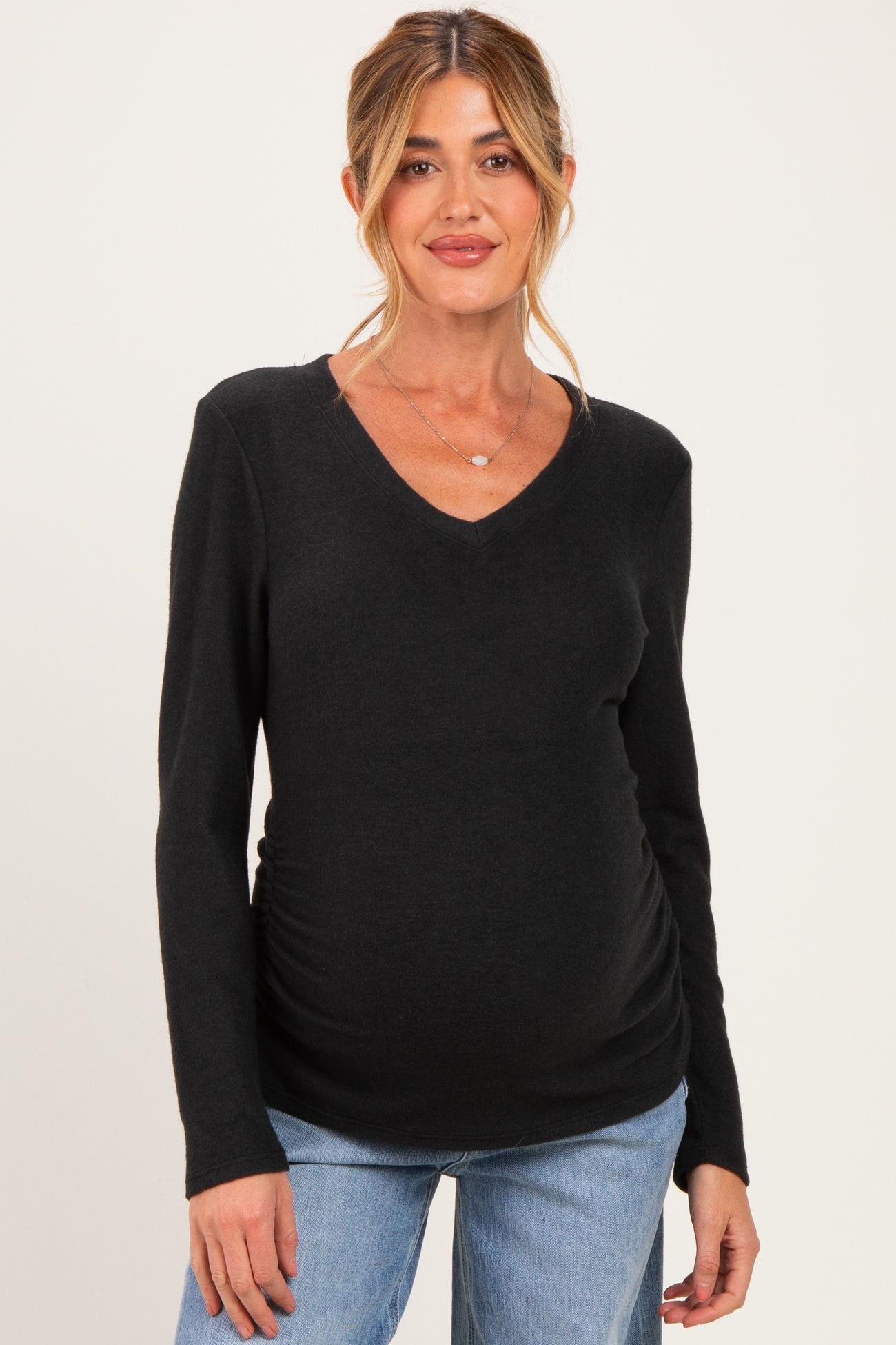woman wearing a black long sleeve maternity top with a v-neck and ruching on the sides, showing her baby bump