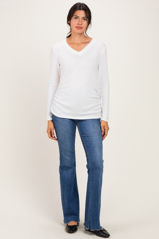 woman wearing a white long sleeve v-neck top with ruched sides and blue flared jeans
