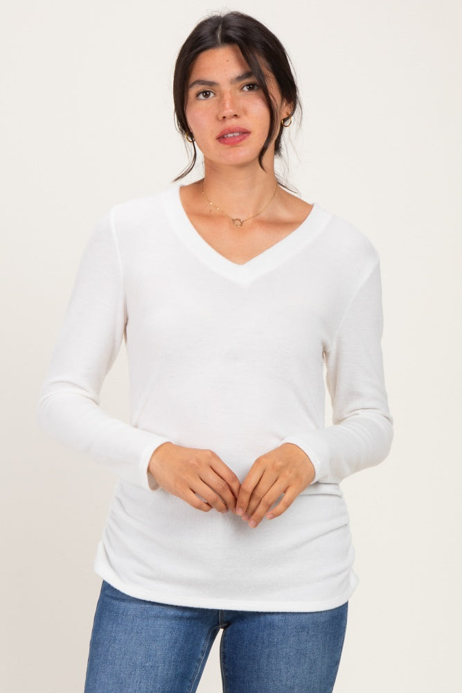 woman wearing a white long sleeve v-neck top with ruching at the sides, paired with blue jeans