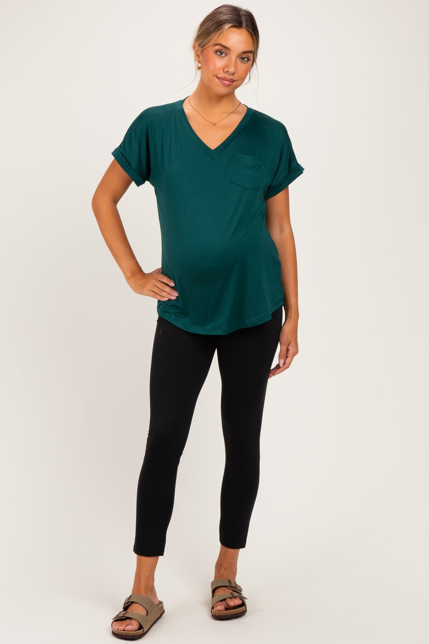 woman wearing a teal maternity top with a pocket and black leggings, showing her baby bump