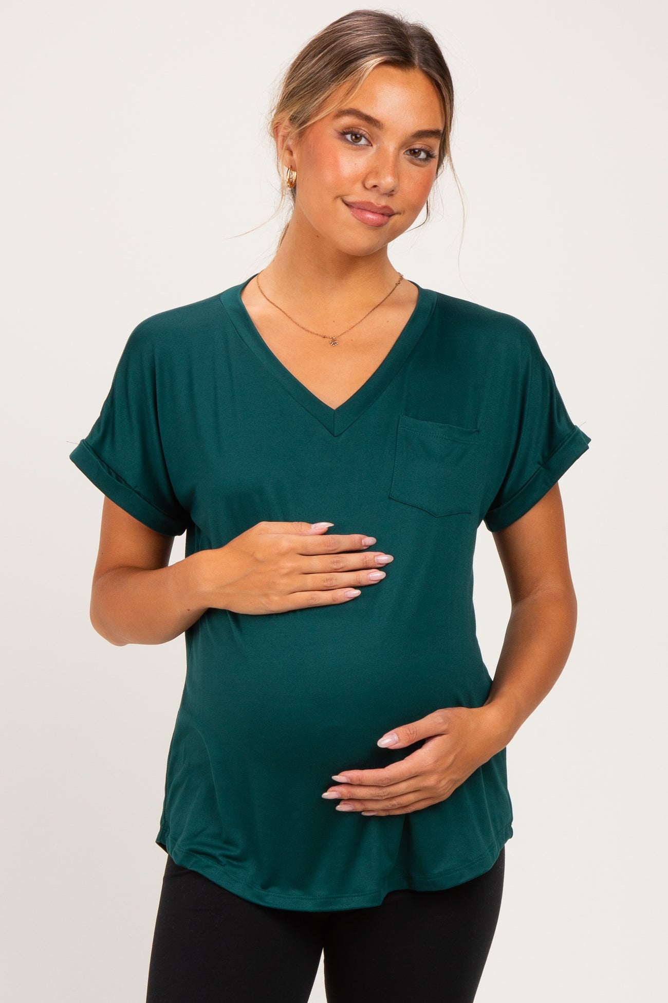 woman wearing a dark green v-neck maternity top with rolled sleeves and holding her baby bump