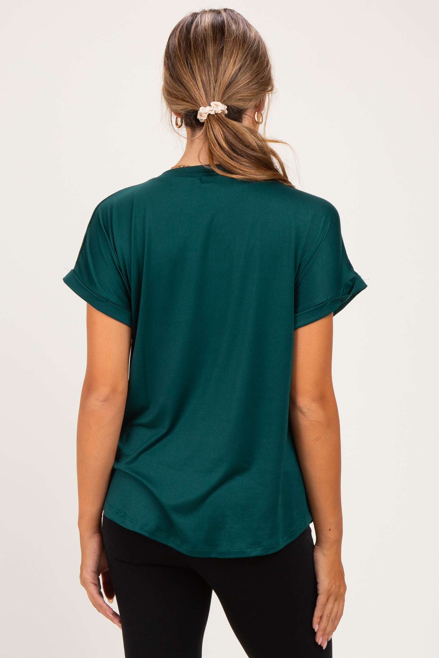 woman wearing a dark green short sleeve maternity top, view from the back with rolled sleeves