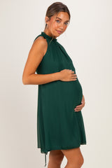 woman wearing a dark green maternity dress with a ruffled neckline and holding her baby bump