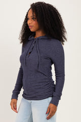woman wearing a navy blue long sleeve hoodie with a button detail and side ruching, styled with light blue jeans