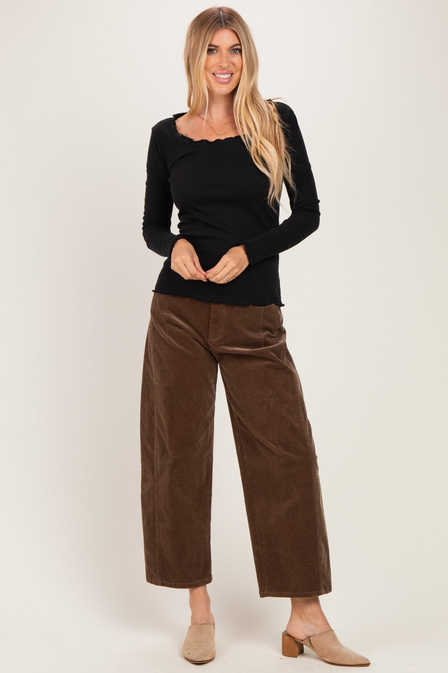 woman wearing a black long sleeve ribbed top with a scalloped neckline and brown wide-leg corduroy pants