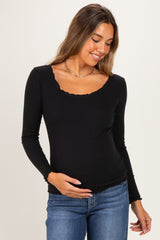 woman wearing a black long sleeve maternity top with a scalloped neckline and holding her baby bump