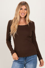 woman wearing a brown long sleeve top with a square neck and scalloped hem, smiling at the camera