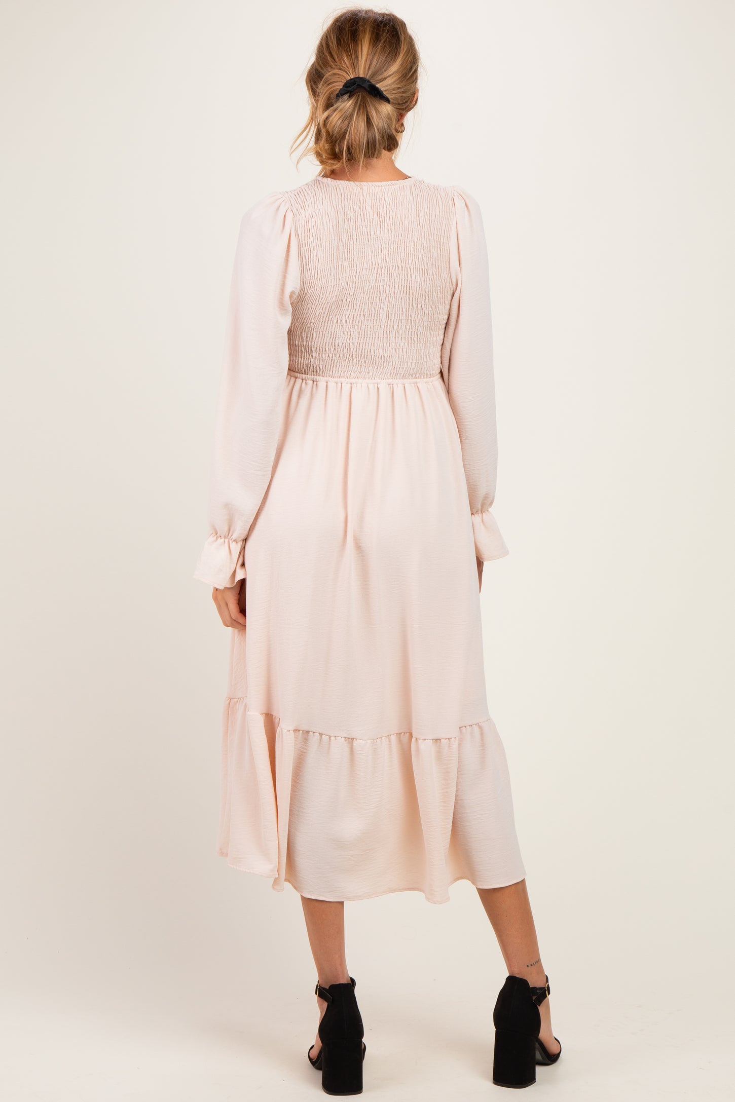 woman wearing a back view of a light pink maternity dress with smocked bodice and long sleeves