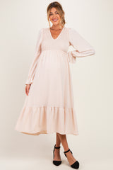 woman wearing a light pink maternity dress with a smocked bodice and long sleeves, holding her baby bump